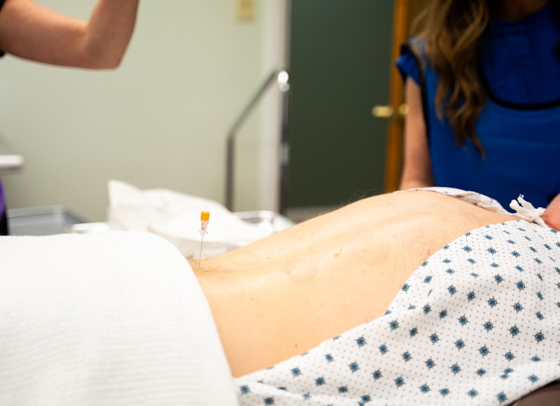 A metal tray holds promotional materials for Botox for Chronic Migraine, including two boxes of onabotulinumtoxinA, three syringes with orange caps, and several informational cards and brochures. One prominent card advertises that eligible, commercially insured patients may pay as little as $0 for Botox treatments and encourages enrollment and scanning a QR code to start saving.
